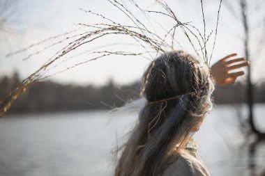 Close up looking at lake woman with long willow twigs crown portrait picture. Closeup rear view photography with blurred background. High quality photo for ads, travel blog, magazine, article