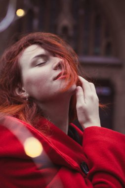 Close up sensual woman in red coat on street portrait picture. Closeup side view photography with old building on background. High quality photo for ads, travel blog, magazine, article