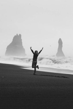 Excited tourist on empty black beach monochrome scenic photography. Picture of person with rocks on background. High quality wallpaper. Photo concept for ads, travel blog, magazine, article