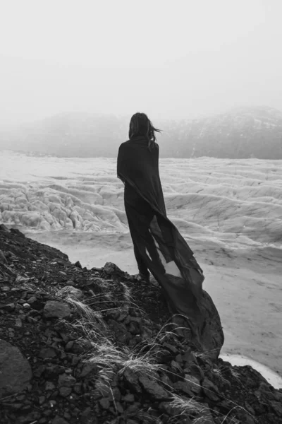 Lady wrapped with gentle fabric on cliff monochrome scenic photography. Picture of person with old glacier on background. High quality wallpaper. Photo concept for ads, travel blog, magazine, article