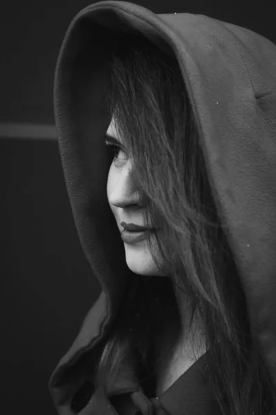 Close up pretty young woman wearing coat with hood monochrome portrait picture. Closeup side view photography with grey background. High quality photo for ads, travel blog, magazine, article