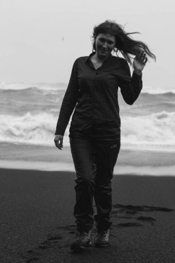 Tourist on black beach at strong wind monochrome scenic photography. Picture of person with sea waves on background. High quality wallpaper. Photo concept for ads, travel blog, magazine, article