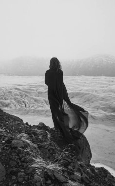 Lonely woman with fabric cape on rock monochrome scenic photography. Picture of person with ancient iceberg on background. High quality wallpaper. Photo concept for ads, travel blog, magazine, article