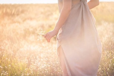 Close up woman with flowers surrounded by sunlight glare concept photo. Side view photography with blooming meadow on background. High quality picture for wallpaper, travel blog, magazine, article