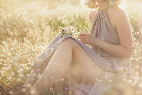 Close up young woman with bouquet sitting in wildflower meadow concept photo. Side view photography with sun glare on background. High quality picture for wallpaper, travel blog, magazine, article