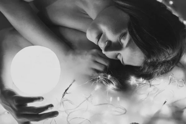 Close up sensual woman with illuminated sphere monochrome portrait picture. Closeup side view photography with fairy lights on background. High quality photo for ads, travel blog, magazine, article