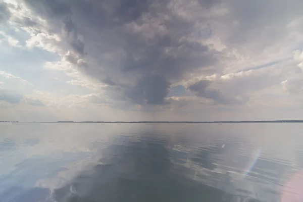 Gloomy clouds on smooth water surface landscape photo. Beautiful nature scenery photography with horizon on background. Seascape. High quality picture for wallpaper, travel blog, magazine, article