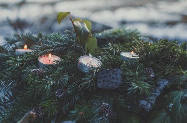 Close up tealight candles in evergreen pine branches concept photo. Front view photography with blurred wintertime background. High quality picture for wallpaper, travel blog, magazine, article