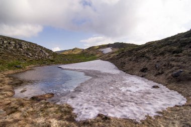 Melting ice puddle in spring mountains landscape photo. Beautiful nature scenery photography with sky on background. Ambient light. High quality picture for wallpaper, travel blog, magazine, article