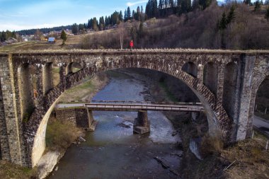Woman standing on brick bridge in Dragobrat landscape photo. Nature scenery photography with spruces on background. Ambient light. High quality picture for wallpaper, travel blog, magazine, article