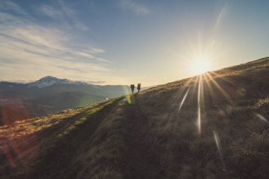 Sırt çantalı yürüyüşçüler tepenin yamacında yürüyorlar. Arka planda güneş olan doğa fotoğrafçılığı. Çevre ışığı. Duvar kağıdı, seyahat günlüğü, dergi, makale için yüksek kaliteli resim