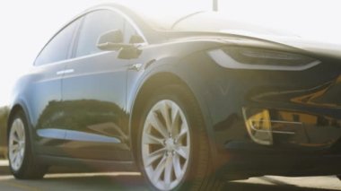 Elektrikli araba yükleniyor. Elektrikli araçlar için alternatif enerji. Günbatımında modern lüks siyah araç. Elektrikli SUV arabası. Çevre dostu yeşil çevre kavramı.