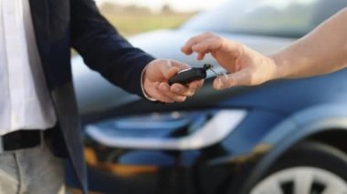 Adam arabanın anahtarlarını alıcıya veriyor. Elektrikli araba galerisindeki adamlar satın alınmış arabaların arka planında el sıkışıyorlar. İş adamı otomobil galerisinde beyaz bir adama araba anahtarı veriyor.