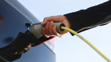 Bir elektrikli aracın şarj istasyonundan bağlantısını kesen tanımlanamayan bir adama yaklaş. Elektrikli araba şarjı. Erkek el güç bağlantısını EV vagonuna bağlıyor. Yeşil enerji kavramı