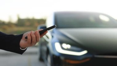 Lviv, Ukrayna - 17 Ekim 2022: Premium sınıf Tesla ekose otomobilin uzaktan kumandası için akıllı telefon uygulaması kullanan tanınmaz bir adam, sürücü uzaktan arabaya yaklaşıyor ve kapıyı açıyor, akıllı araba.