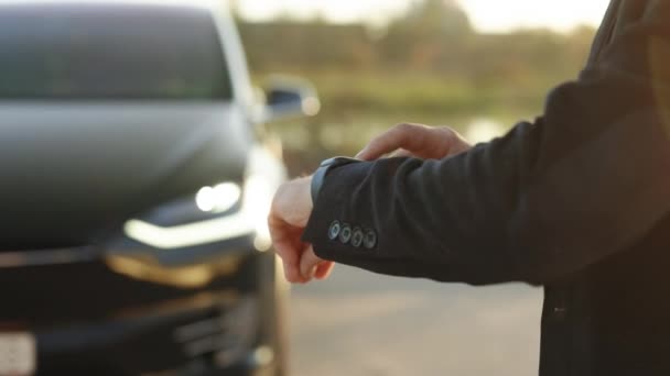 プレミアムクラスの電気自動車 ドライバーの遠隔制御のためのスマートウォッチアプリを使用して認識できないエレガントな男遠く車に近づいてドア スマートカー — ストック動画