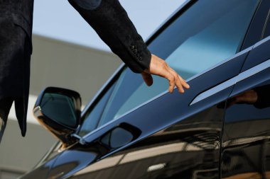 Close up of handsome businessman who walks to electric car. He opens door and gets inside. Business person. Successful people. Luxury lifestyle. Positive mood. Wealth. clipart