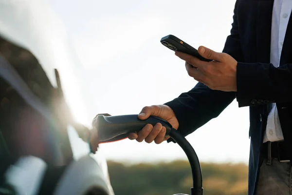 Tanımlanamayan Işadamı Akıllı Telefondaki Uygulamayı Kullanarak Elektrikli Arabayı Şarj Istasyonundan — Stok fotoğraf