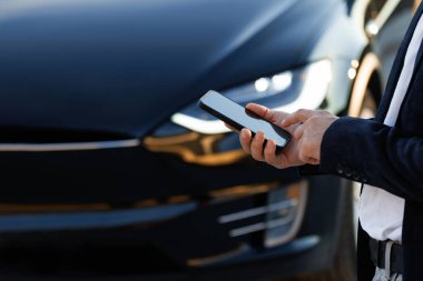 Lviv, Ukrayna - 17 Ekim 2022: Premium sınıf Tesla ekose otomobilin uzaktan kumandası için akıllı telefon uygulaması kullanan tanınmaz bir adam, sürücü uzaktan arabaya yaklaşıyor ve kapıyı açıyor, akıllı araba.