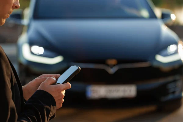 Unrecognizable person controls a self-driving electric car using mobile application. Autonomous autopilot driverless car. Smartphone app. Sensor scanning road ahead for vehicles, danger, speed limits.