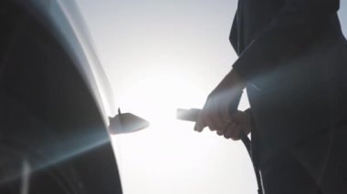 3D animasyon. İşadamı elektrikli arabaya elektrik kablosu bağlıyor. Elektrikli araç şarj bölmesi. Tanımlanamayan adam akıllı telefon uygulaması kullanarak şarj istasyonunda elektrikli araba yüklüyor.