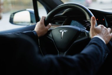 Lviv, Ukrayna - 17 Ekim 2022: Tesla arabasının yeni modelini kullanan işadamı, ön GPS monitörünü kullanarak Tesla aracını sürerken arka görüş. Otomatik pilot kullanan erkek sürücü.