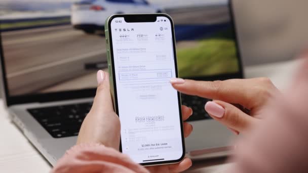 California 2022年11月14日 テスラモデルXプレイを注文 テスラ車をオンラインで購入する意図でスマートフォンのショッピングを使用して女性の手の閉鎖 — ストック動画