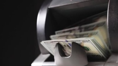 Automatic mechanism for bank financial operations. Currency counting machine counts 100 dollar bills USD banknotes. Cash bill counter money machine stands on scattered dollars. Finance concept.