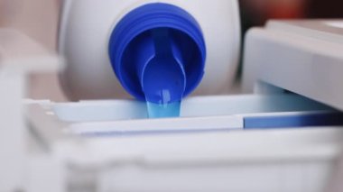 Kadın, büyük şişeden çamaşır makinesinin kompartımanına gerekli miktarda sıvı deterjan döküyor. Ev işleri konsepti