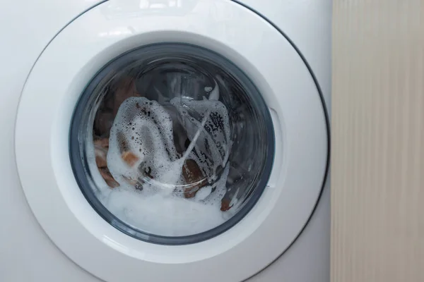 Washing clothing in domestic washing machine in home. Close-up of spinning drum washing machine. White washing machine washes dirty clothes.