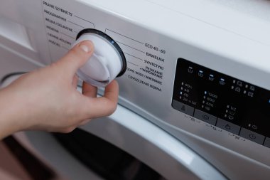 Laundry Setting Washing Machine Dial to ECO Mode for Energy Saving and Environmental Conservation in Bathroom. Close Up Shooting with a Hand Rotating the Front Panel Button the Laundry Machine.