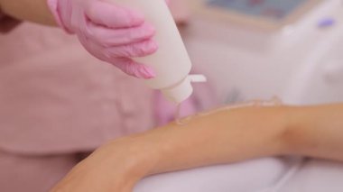 Lazer tüy çıkarma işleminden önce şeffaf bir jel sürüyorum. Güzellik salonunda bir kadının ellerinin epilasyon geçirmesine yakın çekim. Cilt bakımı, kozmetik prosedürleri..