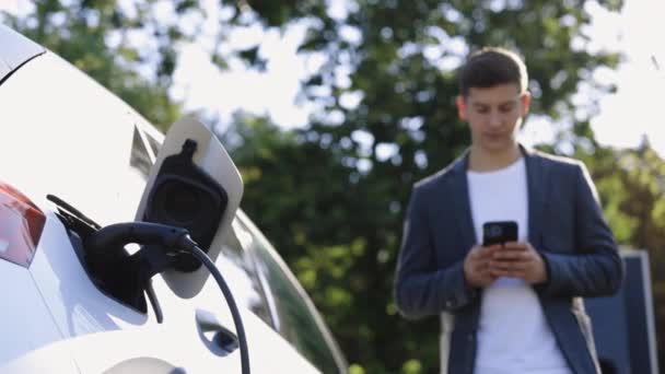 Kaukaski Biznesmen Korzystający Smartfona Czekający Podłączenie Zasilania Pojazdów Elektrycznych Ładowania — Wideo stockowe