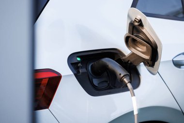 Elektrikli araç modern EV 'yi şarj ediyor. Ekoloji alternatif enerjisini geleceğin sürdürülebilir enerjisinden koru. Şehrin caddesindeki otoparkta elektrik kablosuyla şarj edilen modern elektrikli araba.