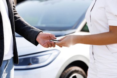 Adam arabanın anahtarlarını alıcıya veriyor. Alınan arabaların arka planında tanınmayan insanlar elektrikli araba bayisinde el sıkışıyor. İş adamı otomobil galerisinde kadına araba anahtarı veriyor.