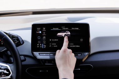 Modern elektrikli otomobiller için akıllı multimedya dokunmatik ekran sistemi kullanan bir erkek parmak. Yeşil enerji, sıfır emisyonlu araba iç görünümü. Uzun menzilli elektrikli araç.