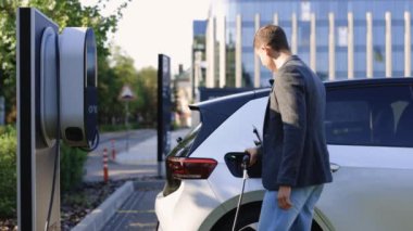 İşadamı elektrikli arabanın fişini çekiyor. Lüks elektrikli araba dolu. Elektrik güç dolumu yarışması ve kablo bağlantısı koptu. Ekoloji alternatif enerjisini gelecek sürdürülebilir olarak kaydet.