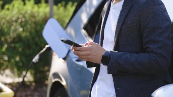 Biznesmen Korzystający Smartfona Czekający Podłączenie Zasilania Pojazdów Elektrycznych Ładowania Akumulatora — Wideo stockowe