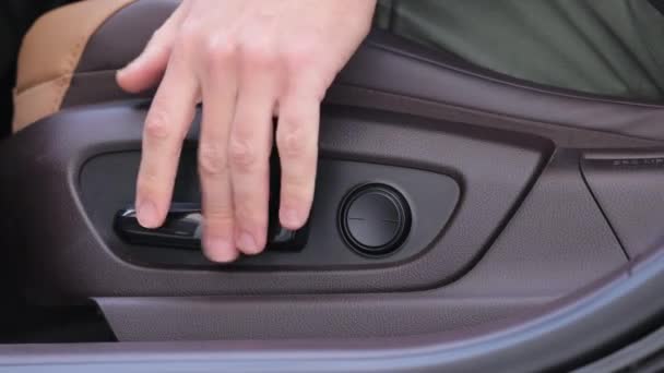 ドライバーシート調整ボタン 座席位置を調整するためのボタン 車内インテリア 男性の手は家具の調節ボタンの動きの活動化したパワー シートの高価なブラウン レザーを押します — ストック動画