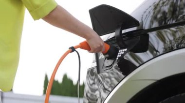 Tanımlanamayan bir kadın elektrikli araba kablosunun fişini çekiyor. Kadın elleri elektrik kablosunu koparıp elektrikli arabayı şarj ediyor. Çevre dostu alternatif enerji yeşil çevre kavramı.