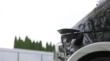 Elektrikli araba ya da elektrik şarj istasyonunda EV fişi takan kadın. Kadın, elektrik yüklemek için elektrik kablosu veya takılabilir akıllı saat uygulaması kullanarak EV otomobili bağlıyor.