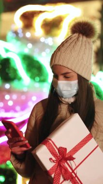 Dikey ekran, maske takmış güzel bir kadın sokakta dikilirken akıllı telefonunda geziniyor. Yılbaşı hediyesi olan genç bir kadın cep telefonundan mesaj atıyor. Kış konsepti