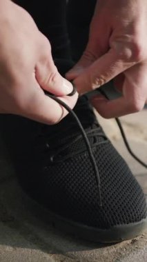 Ayakkabı bağcıklarını bağlayan adamın dikey format videosu. Spor ayakkabılarına ayakkabı bağlayan erkek eller spor yapıyor..