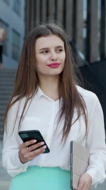 Modern akıllı telefon kullanarak beyaz gömlek giyen güzel iş kadınının dikey format videosu. Profesyonel bayan işveren dışarıda cep telefonundan mesaj yazıyor..