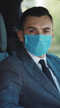 İş adamı sağlık hizmetlerinin dikey videosu. Salgın. Vatandaşlar. Güvenlik kilidi. Coronavirus 'u önlemek ve arabasına binmek için tıbbi maske takan bir iş adamı.