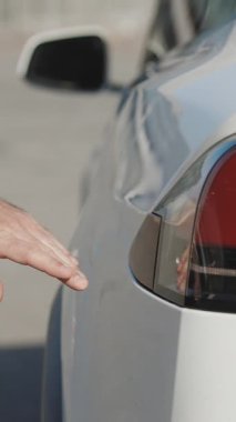 Elektronik araba şarj istasyonunda elektrikli arabanın fişini takan tanımlanamayan bir adamın dikey videosu. Lüks beyaz elektrikli araba şarj oluyor. Çevreye duyarlı erkek elektrikli araç yüklüyor.