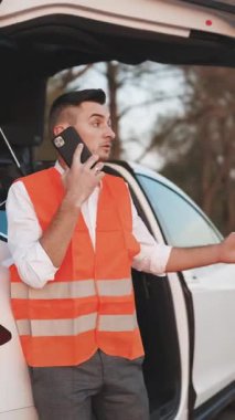 Mutsuz iş adamının, bozuk elektrikli arabanın yanında telefonla konuşurken çekilmiş dikey videosu acil durum sigortası sorununun çözümüne yardımcı oluyor. Adam araba yardım servisini arıyor. Trafik kazası. Onarım