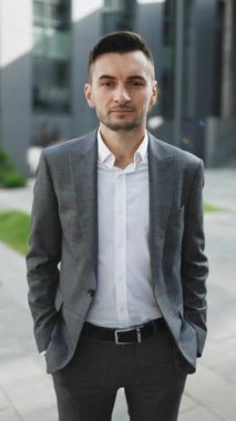 İş dışında duran takım elbiseli yakışıklı girişimcinin dikey videosu. Başarılı bir iş adamı. Kurumsal insanlar. Ofis müdürü. İş adamı iş merkezinin yakınındaki kameraya bakıyor..