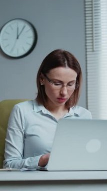 Profesyonel bir kadının dizüstü bilgisayarını kullandığı dikey format videosu ofis masasında oturuyor, mutlu bayan müşteri çevrimiçi internet sitesini doğruluyor