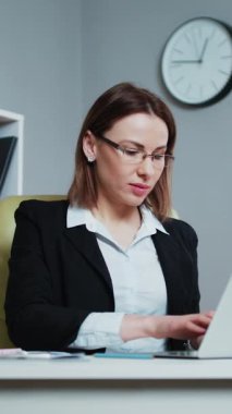 Tişörtlü çekici bir iş kadınının modern ofis arka planında gülümseyen ve kameraya bakan portresinin dikey hali..